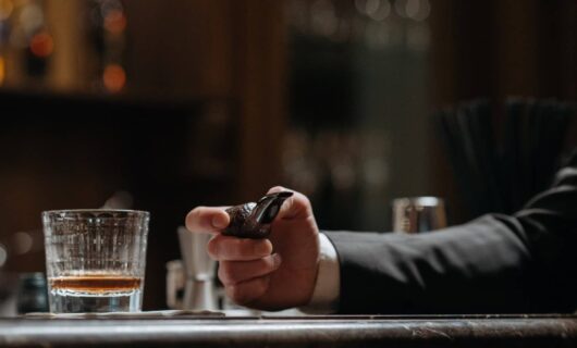 Bicchiere di Whiskey vicino a una persona con la pipa